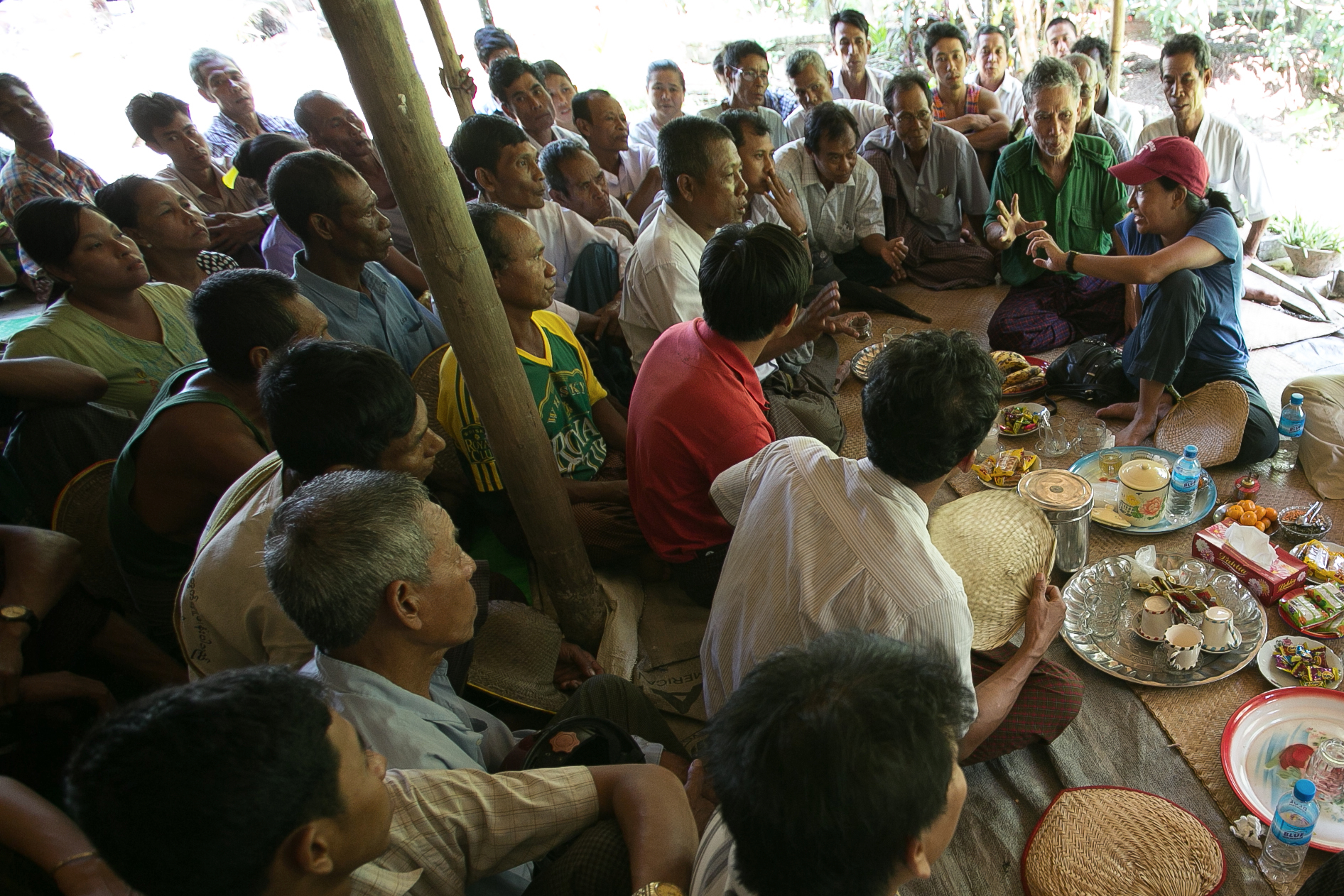 Photograph © Tim Mitzman for Proximity Designs 2013 Debbie Aung Din Taylor (with red hat), co-founder of Proximity Designs, meets with villagers in A Phaung Gyi, in Dedaye township in the Ayeyarwaddy River Delta. Many of the villagers use crop loans provided by Proximity Designs to plant rice. It also provides agricultural advice, and now distributes a line of popular, low-cost solar lights (90 percent of Myanmar's rural households are not on an electrical grid).
