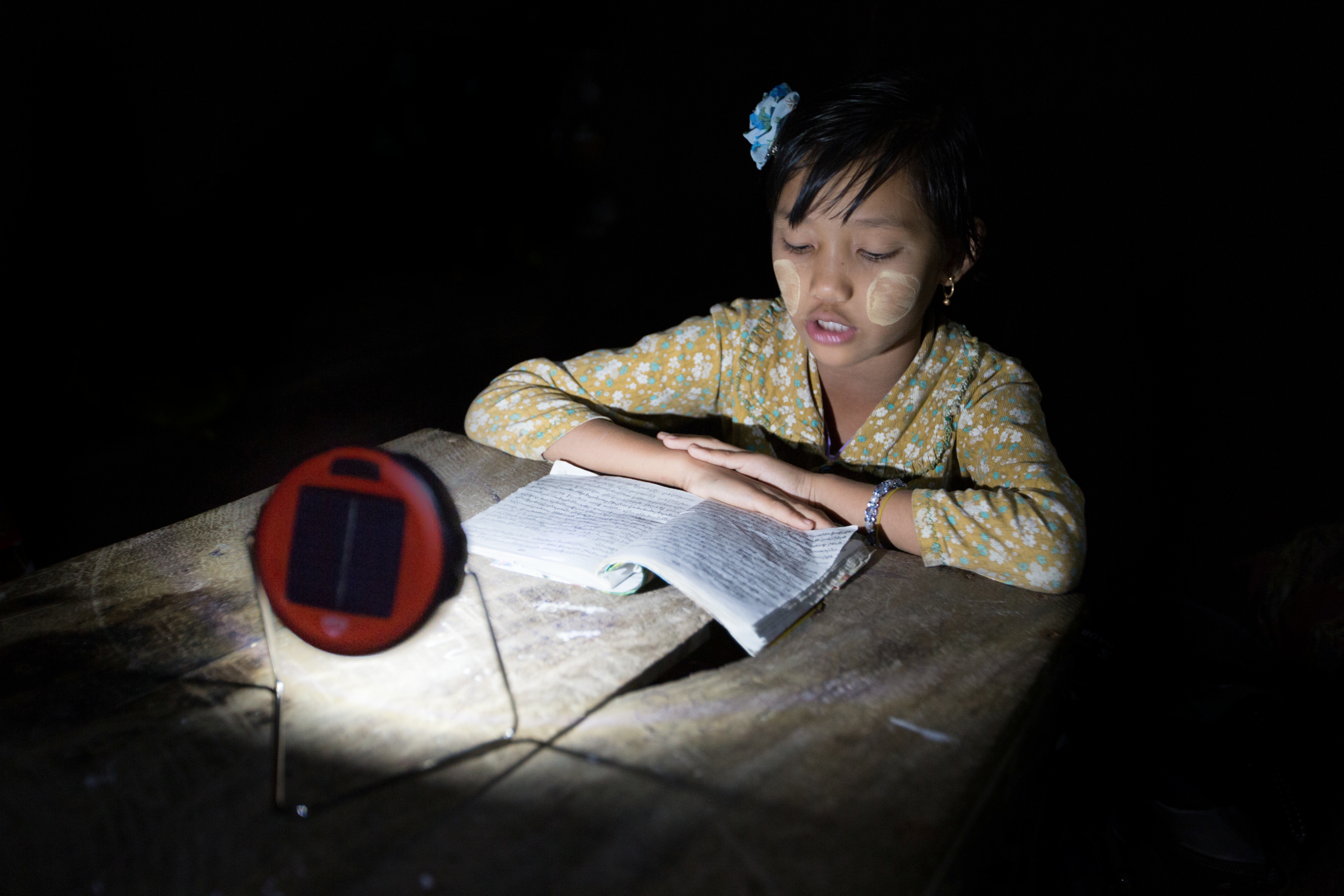 Photograph © Tim Mitzman for Proximity Designs 2013 Proximity Designs now sells d.light solar lights—typically, on a multimonth installment plan. The basic light, shown here, has the most basic of uses: enabling reading, or homework, at night, in lieu of candles, which are expensive, a fire hazard in bamboo houses, and unsuitable for use under mosquito netting. (The white paste on the girl’s cheeks is <i>thanaka,</i> a cosmetic paste made from ground bark, which many women and girls in Myanmar apply to guard against sunburn and to protect the skin.)