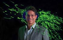 Vamsi Mootha with an image from his lab showing thread-like mitochondria (green) moving within a cell.