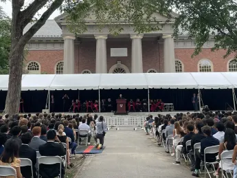 Outdoor convocation ceremony with a crowd seated under a tent, against Memorial Church
