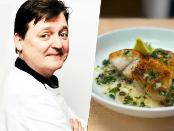 Chef standing confidently with arms crossed, alongside a plated fish dish with herbs.