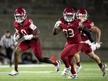 Two football players in red jerseys sprint across the field, showcasing teamwork and determination.