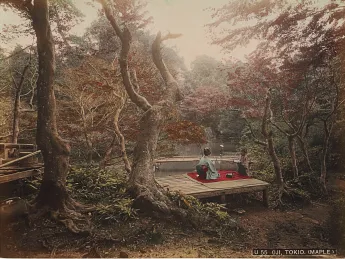 Two women in traditional clothing sitting on a wooden platform near a tranquil pond, surrounded by autumn foliage.