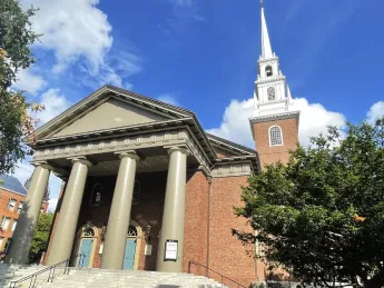 Historic church with a tall steeple, surrounded by trees and a blue sky.