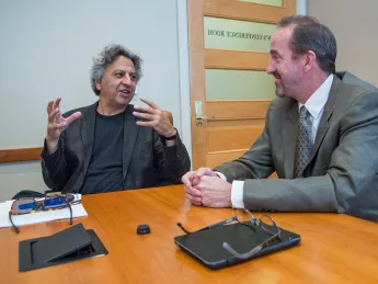 Two men engaged in conversation at a conference table, one gesturing animatedly.