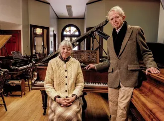 An older couple standing in a large room filled with pianos