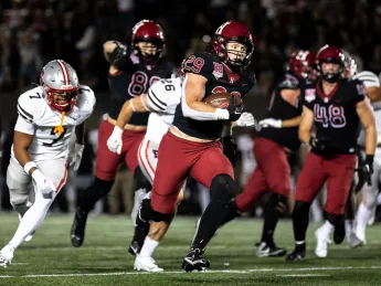 Harvard Football player 29 runs with football with Brown players running after along with other Harvard players