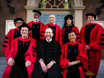 8 people in academic robes sit for a photograph in front on Memorial Church