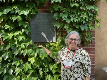 Woman standing next to brick and ivy covered wall with a bronze plaque on the wall
