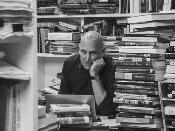 Edwin Frank sits with stacks of books in the background