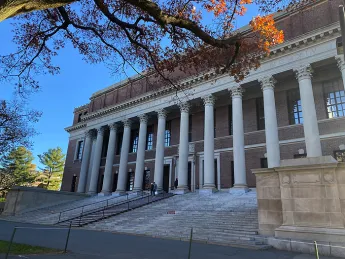 The facade of Widener Library with columns and steps with blue sky and trees