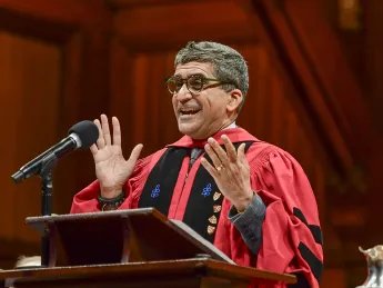 Rakesh Khurana, wearing a red doctoral robe, speaking at a podium 