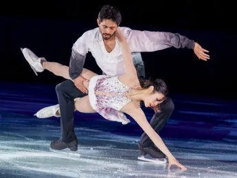 Figure skating pair performs an elegant lift, with the woman extended low and arm reaching toward the ice.