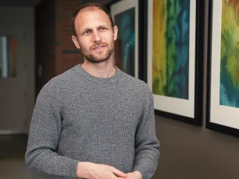 Man in gray sweater standing in hallway with colorful abstract art on wall.