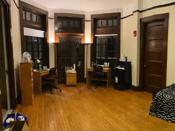 A large dorm room with desk, bed, lamps, and quarantine necessities, including bottled water, masks, and sanitizing supplies.