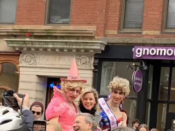 Elizabeth Banks looks at the camera as she rides in a convertible with two members of the Hasty Pudding Theatricals.