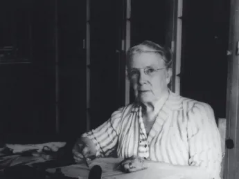 Photograph of a stout middle-aged woman seated at her desk, writing