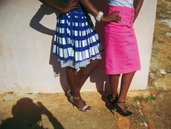 The lower halves of two women stylishly dressed in bright colored skirts and high heels