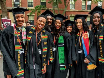 Harvard undergraduates standing happily in Commencement regalia 