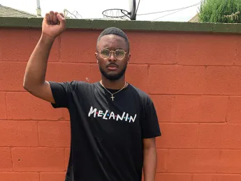 Elijah DeVaughn '21 in black shirt bearing the word "melanin," stands with his right fist raised