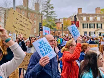A crowd of marchers carry signs that read "We need a fair raise"
