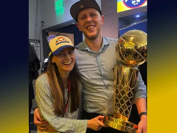 Balcetis smiling and holding the NBA championship trophy, with his arm around his wife