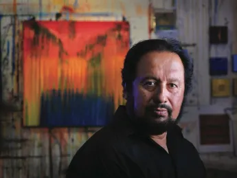 Painter George Oommen in his studio. His painting <em>Visions of Kerala 2</em> (acrylic on  canvas, 2005) hangs behind him. 