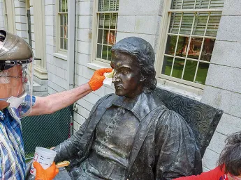 Conservators from Skylight Studios work on the John Harvard statue