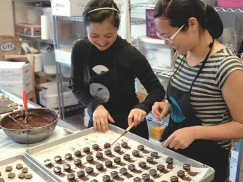 In the Sôcôla kitchen, sisters Wendy (left) and Susan Lieu dip a few dozen chocolate truffles laid out on baking parchment. 