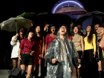 An a cappella group performs in the rain. Despite monsoon-like weather, dozens of student music and dance groups performed in Harvard Yard as part of the evening's program.
