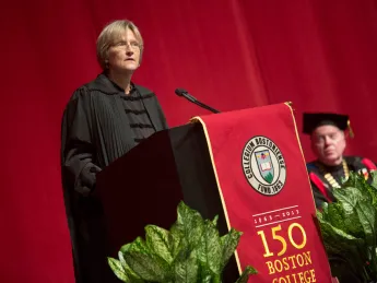 Father William Leahy, Boston College president, looks on as Drew Faust delivers her address at the Boston College sesquicentennial celebration.