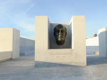 An enlarged version of the famous bronze bust of Roosevelt created by American sculptor Jo Davidson appears at the threshold of a square, white-granite, open-air plaza.