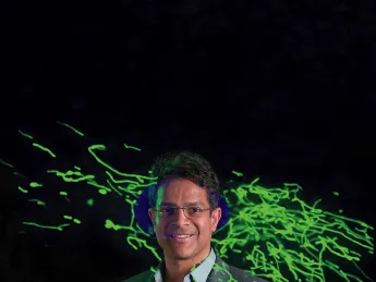 Vamsi Mootha with an image from his lab showing thread-like mitochondria (green) moving within a cell.
