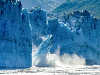 A photograph of a glacier breaking apart in Alaska, with large chunks of ice falling into the ocean.
