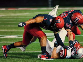 Two Harvard football players tackle a player from Brown.