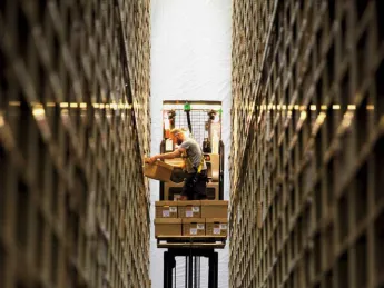 Photograph of worker between two enormously high stacked bookshelves at the Harvard Depository
