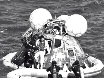 A man in a wetsuit helps an astronaut out of an Apollo capsule floating in the ocean