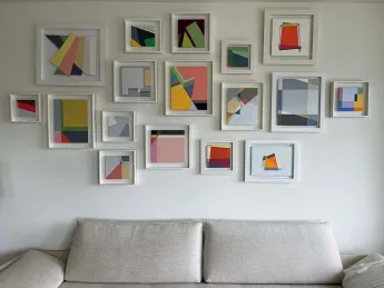 A collection of abstract geometric paintings hang above a white couch