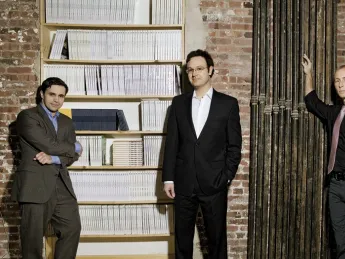 Editors with their product. Left to right, Keith Gessen, Mark Greif, and Chad Harbach of <i>n+1</i> at their Brooklyn office, with a bookcase full of past issues.