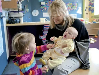Mary Kinsella Scannell, vice president for early education and care, plays with baby Kinsey Ferraguto and toddler Margot Vorhees.