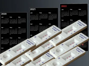 A stack of positive COVID tests in the foreground with 2020-2022 calendars in the background