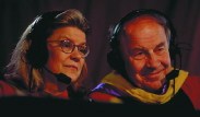 broadcasters (Professors Diana Eck and Dudley Herschbach) in gowns, wearing headsets