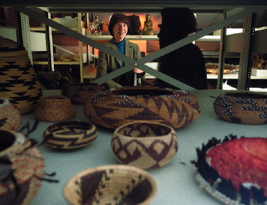 Rubie Watson, director of the Peabody Museum of Archaeology and Ethnology, in a museum storage area. More than 99 percent of the collection is buried treasure, not on display. Around her are objects from Asia. The baskets in the foreground were made by the Pomo Indians of northern California. The Òsun basketÓ or Òdowry basketÓ at right is decorated with feathers from a red-headed woodpecker, and the dark tufts at the edge are quail plumes. The basket was collected at an unknown date and donated to the Peabody in 1905 by George G. Heye.