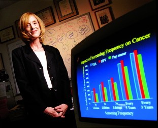 Goldie, standing for a portrait next to a monitor showing the 'Impact of Screen Frequency on Cancer'