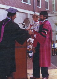 At diploma ceremonies at Dunster House, Master Vorenberg hands a degree to John T. Day Jr., Ph.D. Õ77, now an administrator at Saint Olaf College in Northfield, Minnesota. Day holds his son, Nathaniel.