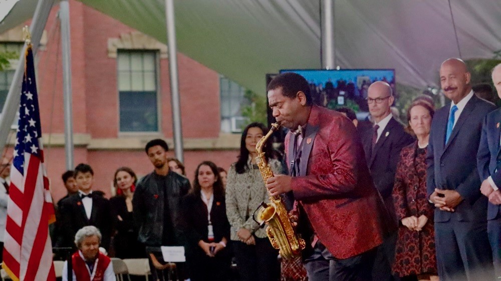 Musician plays the saxophone with audience behind him