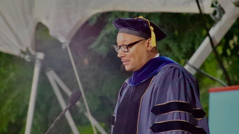 Man in blue faculty robe talks at podium