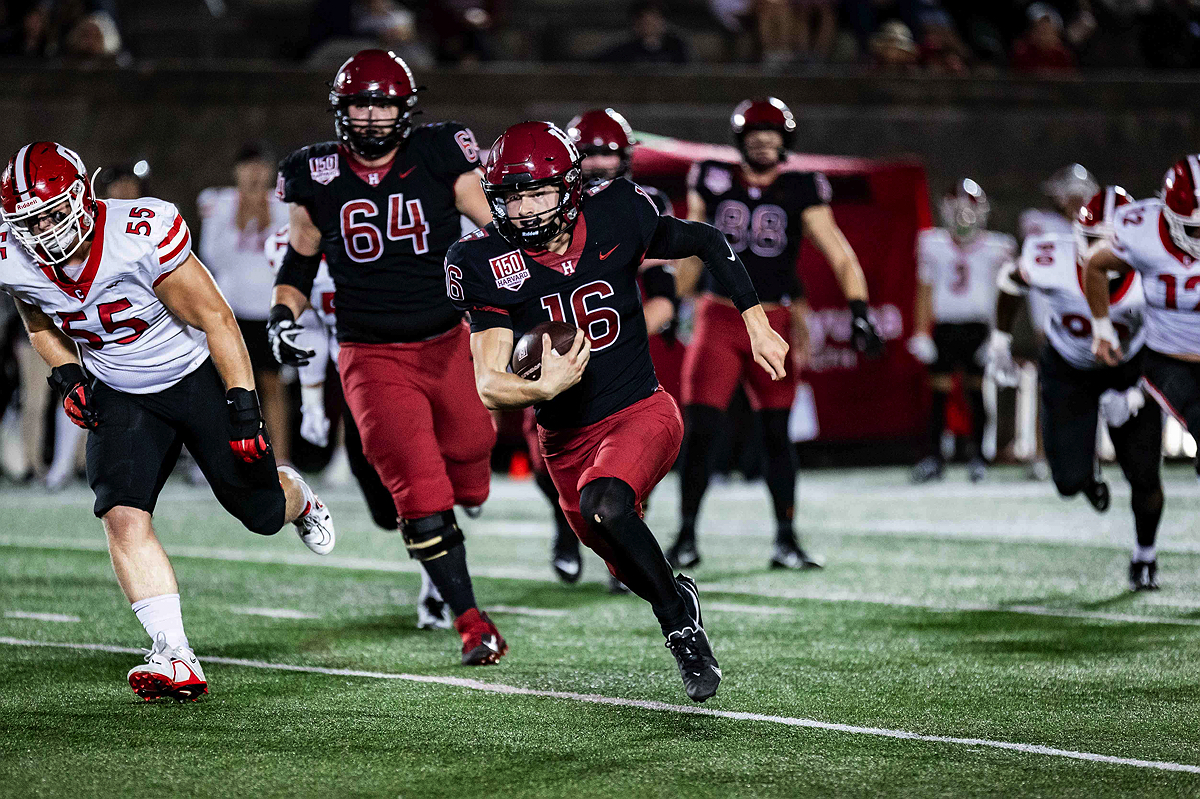 Harvard player runs with ball with teammates behind and Cornell players falling back