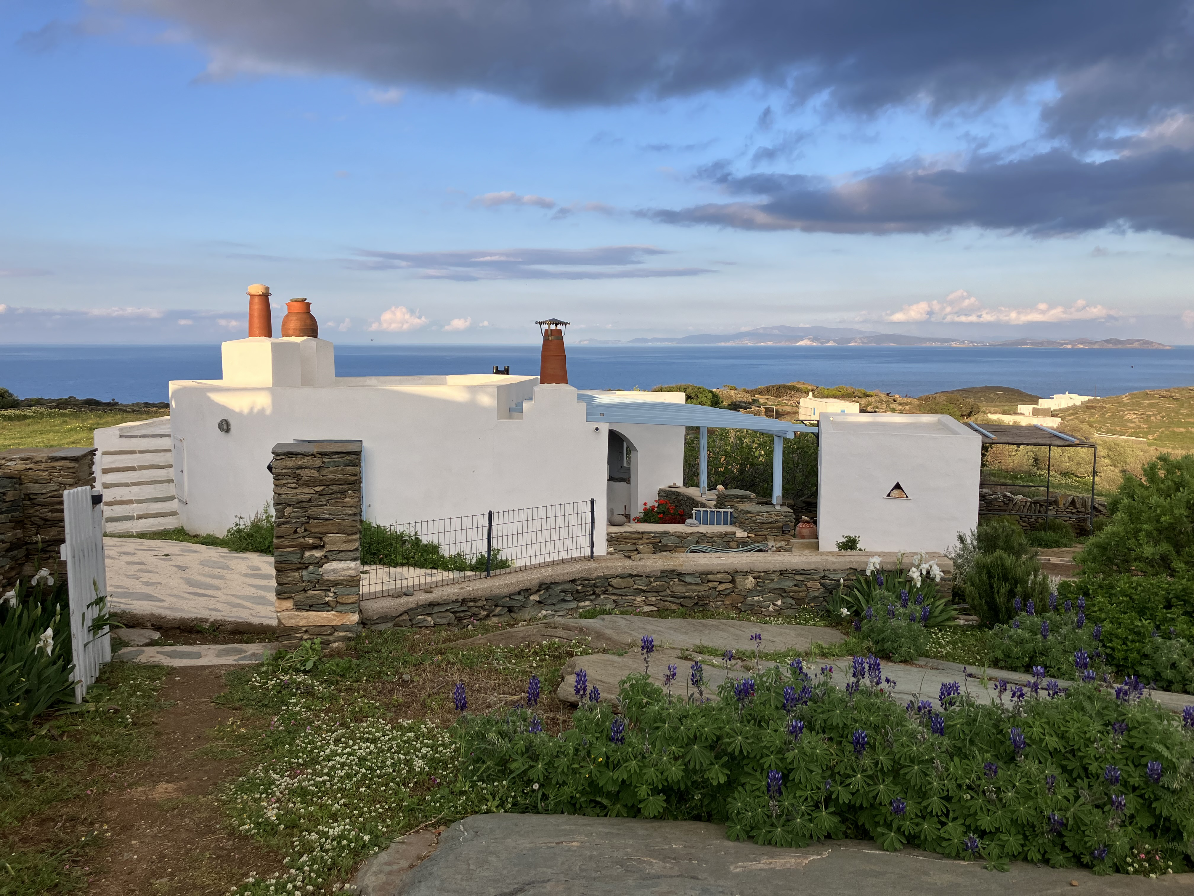 White building with chimneys surrounded by greenery and ocean views under a cloudy sky.