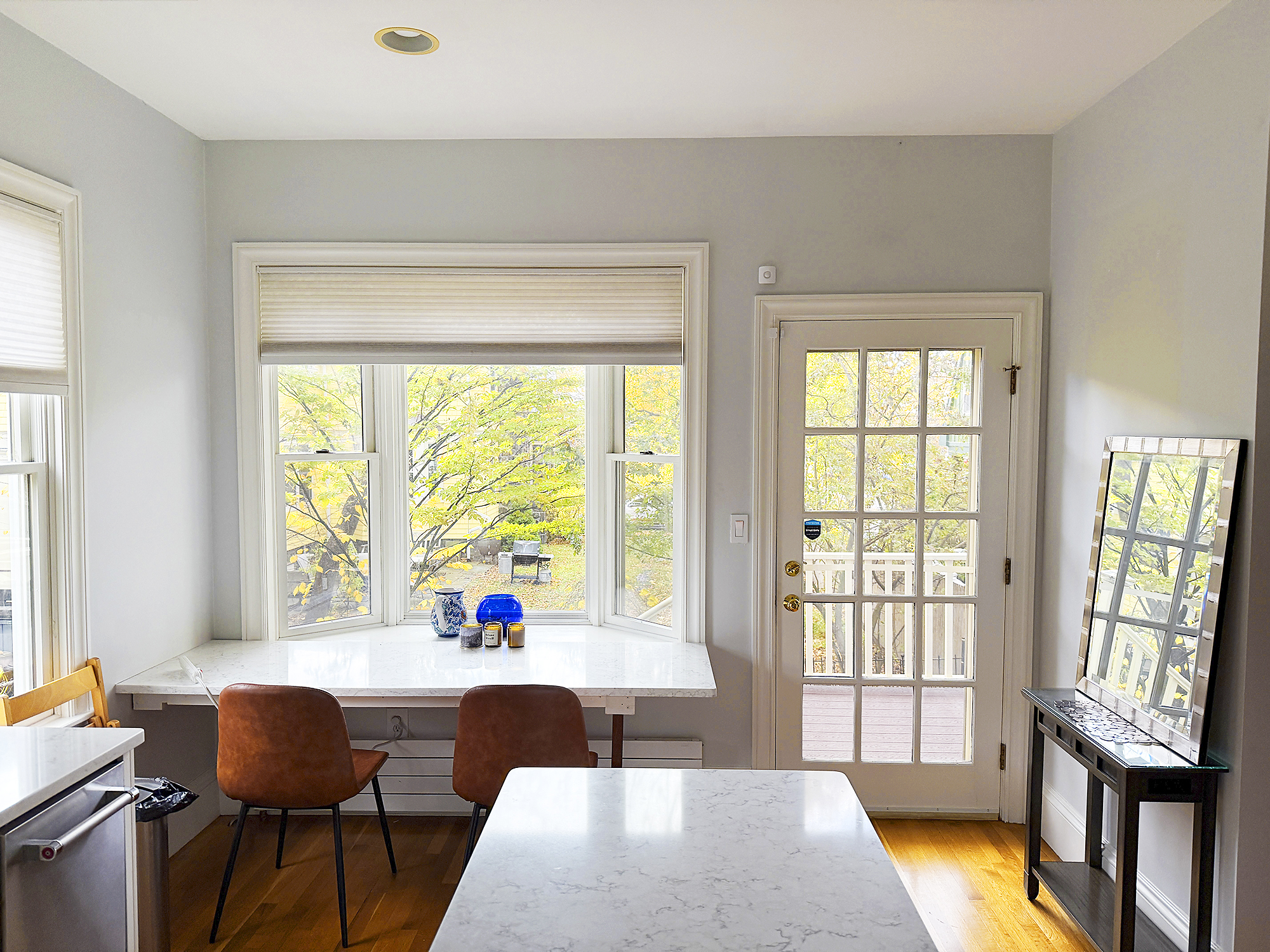 Bright kitchen space with a table, two chairs, and large windows overlooking greenery.